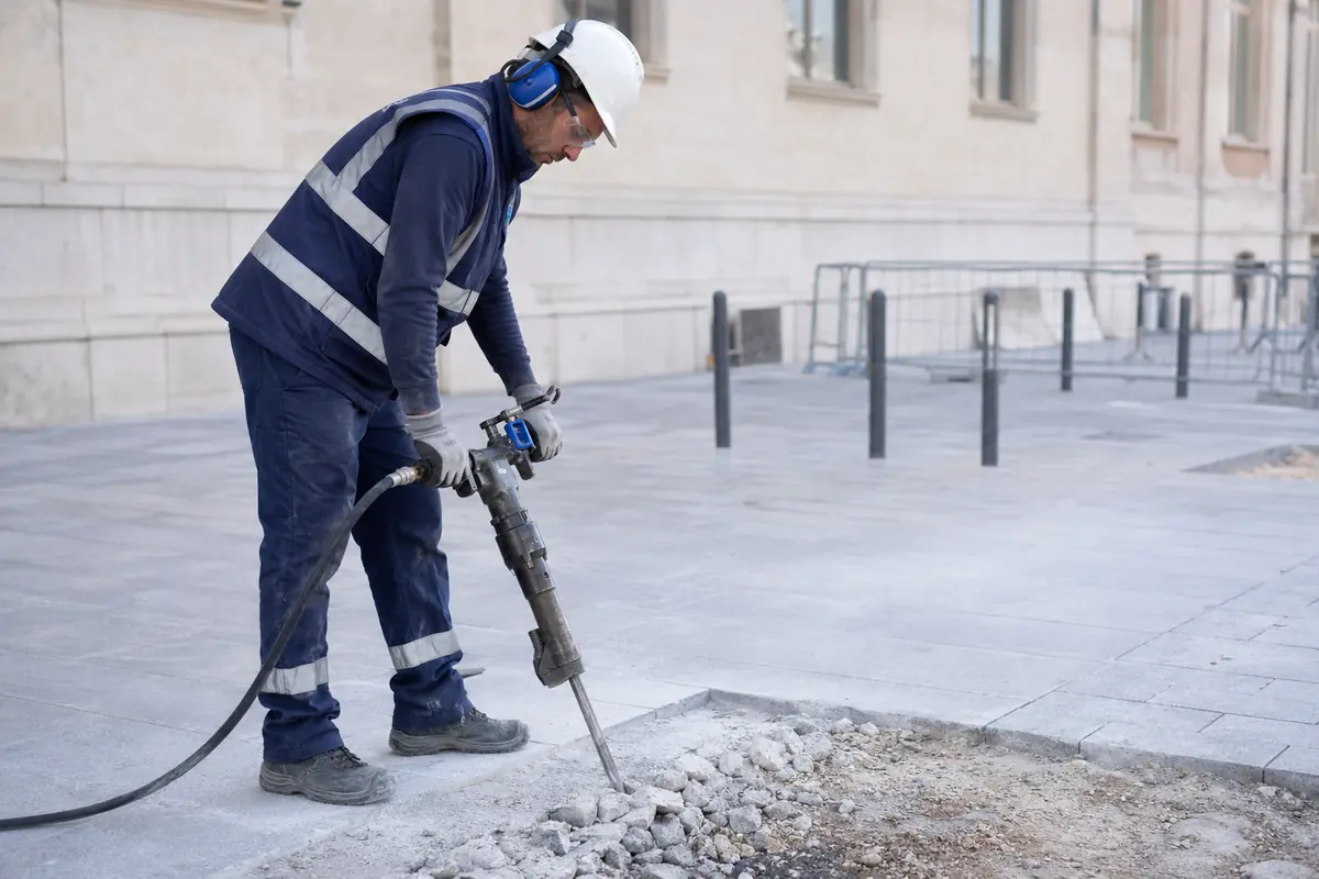 Operario mide vibraciones mano-brazo mientras utiliza un martillo rompedor en una obra urbana.